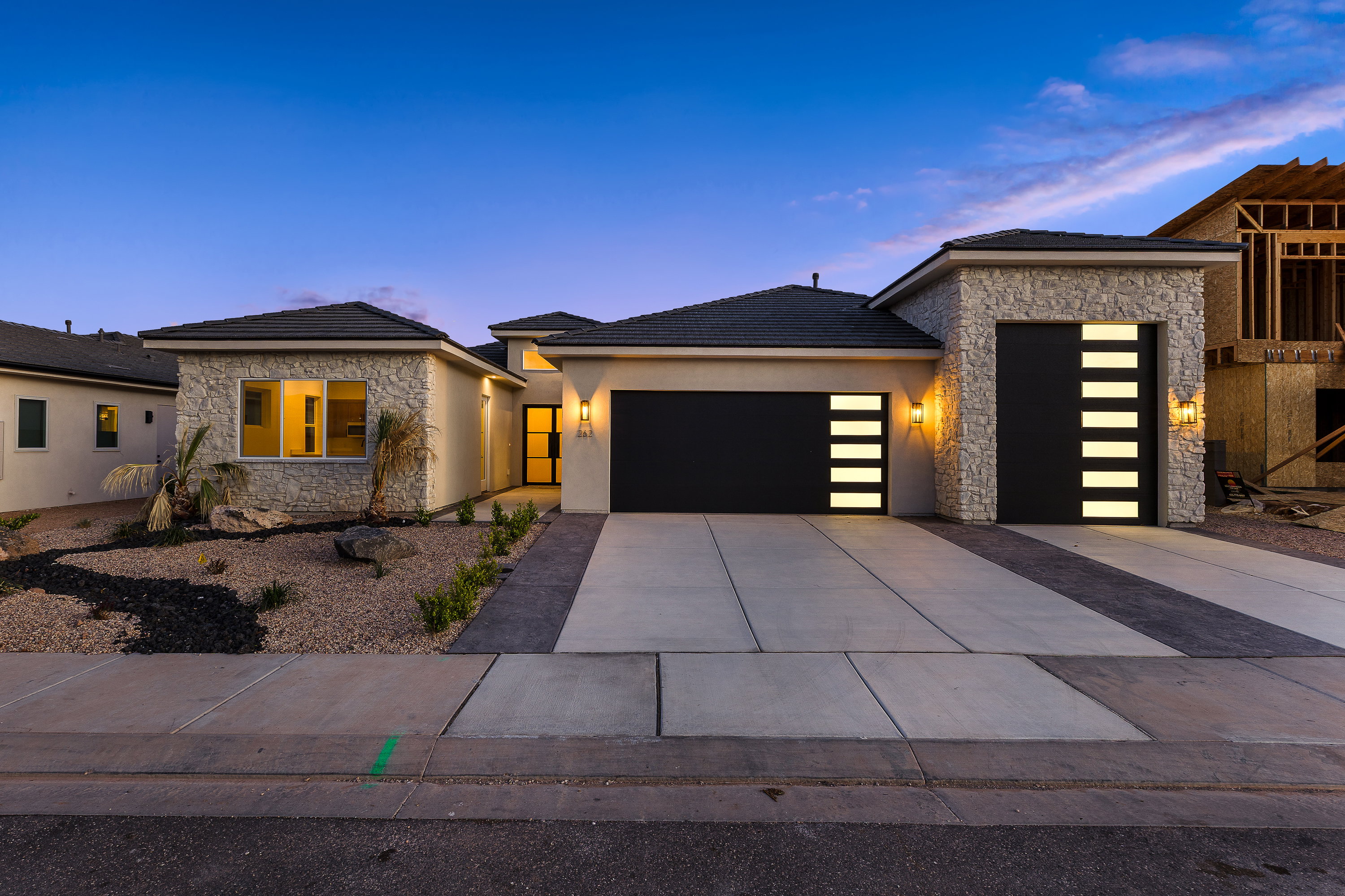 View of front facade with stone siding, a garage, driveway, and stucco siding