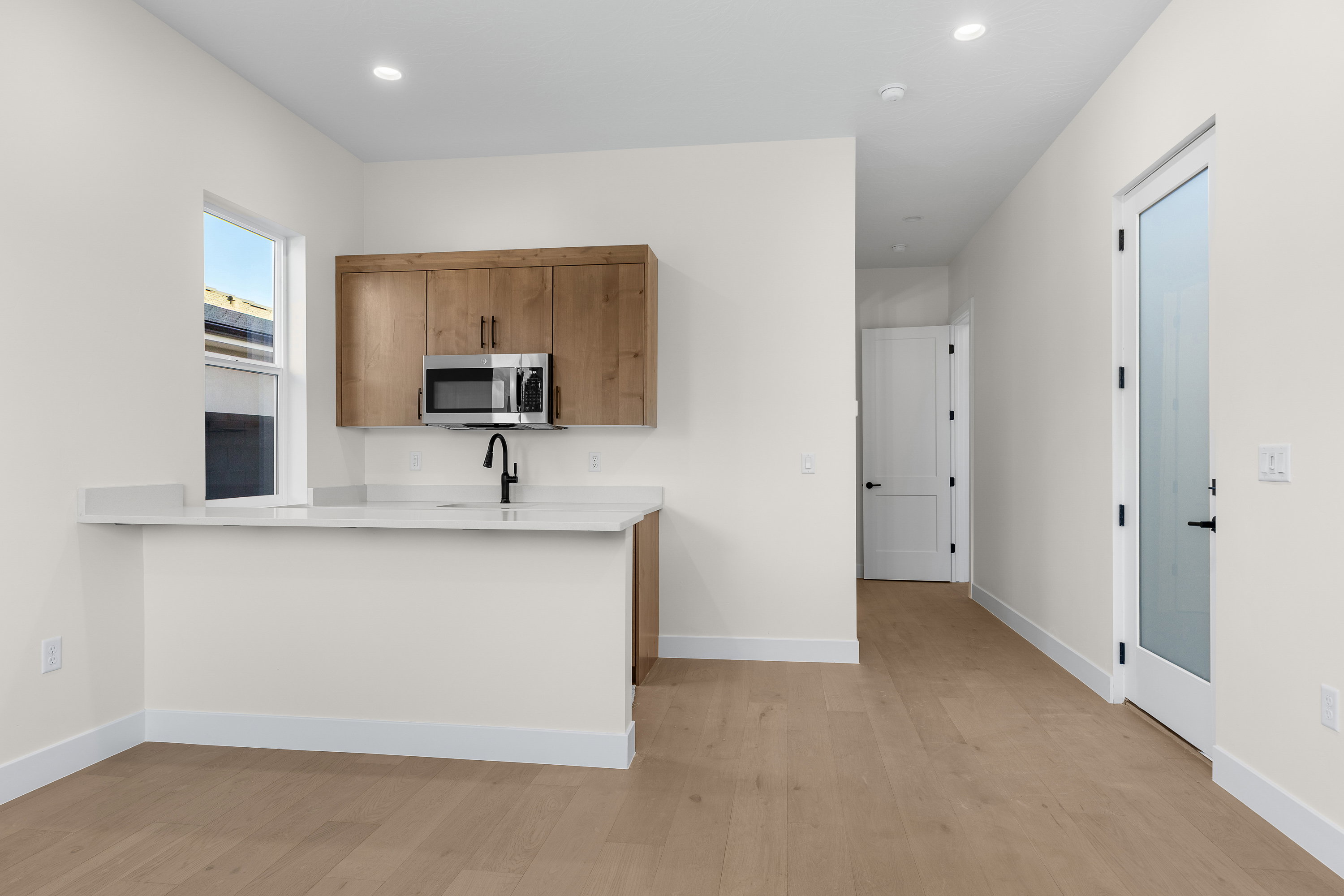 Kitchen with light wood-style floors, stainless steel microwave, a peninsula, wood finish cabinetry, and light stone countertops