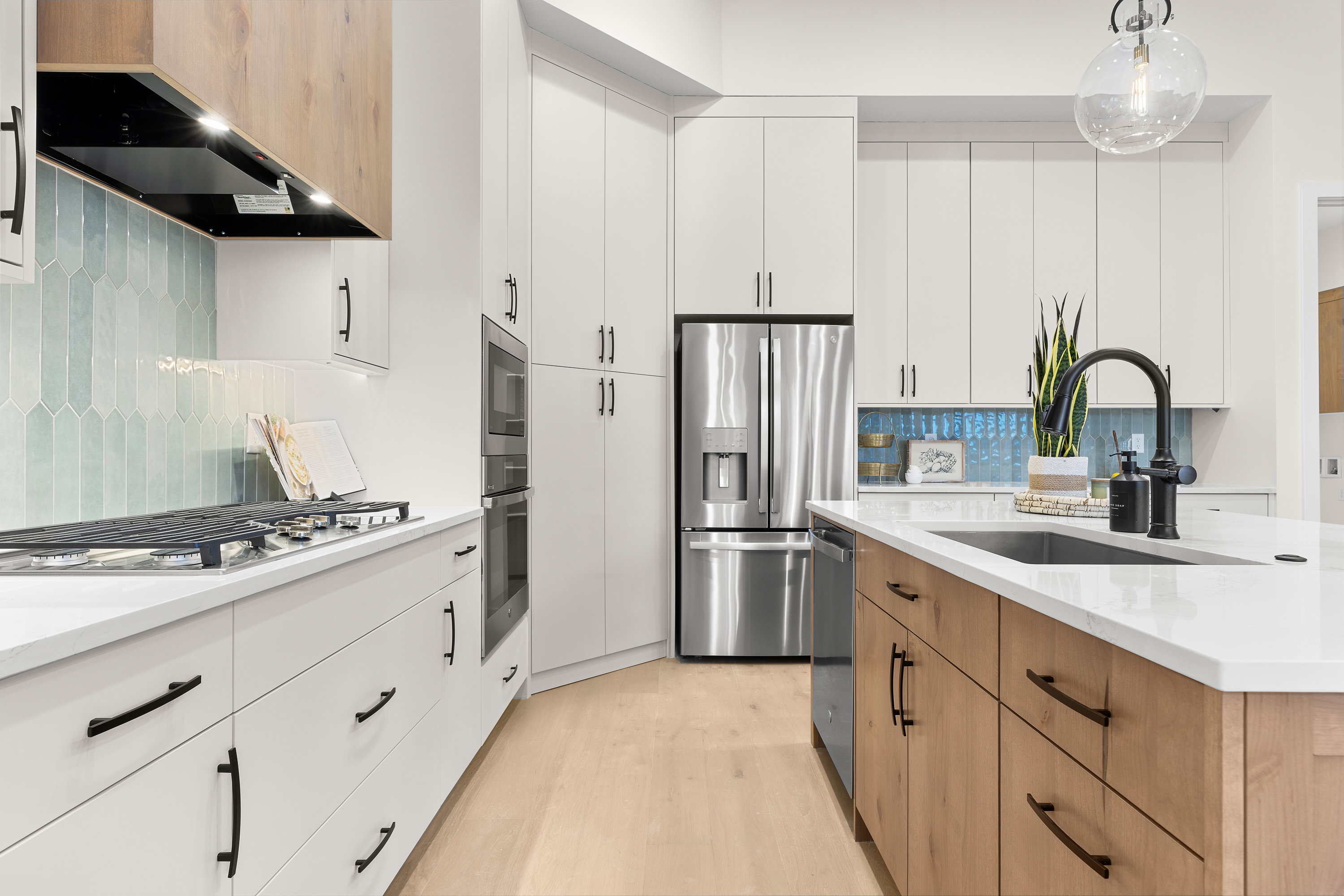 Two tone kitchen featuring two tone cabinetry, decorative backsplash, light stone countertops, decorative light fixtures, and stainless steel appliances