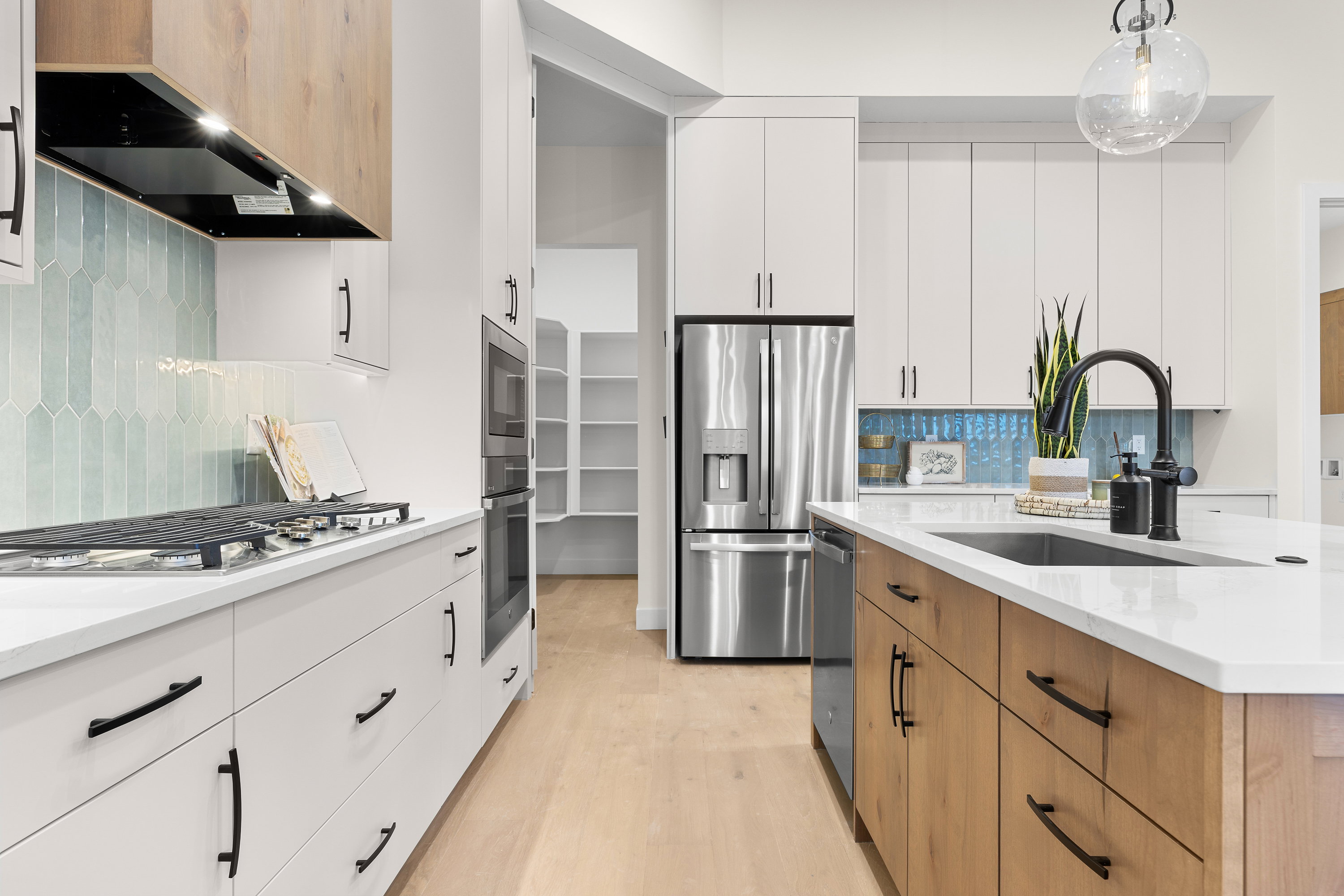 Dual tone kitchen with two tone cabinets, tasteful backsplash, light stone countertops, stainless steel appliances, and hanging light fixtures