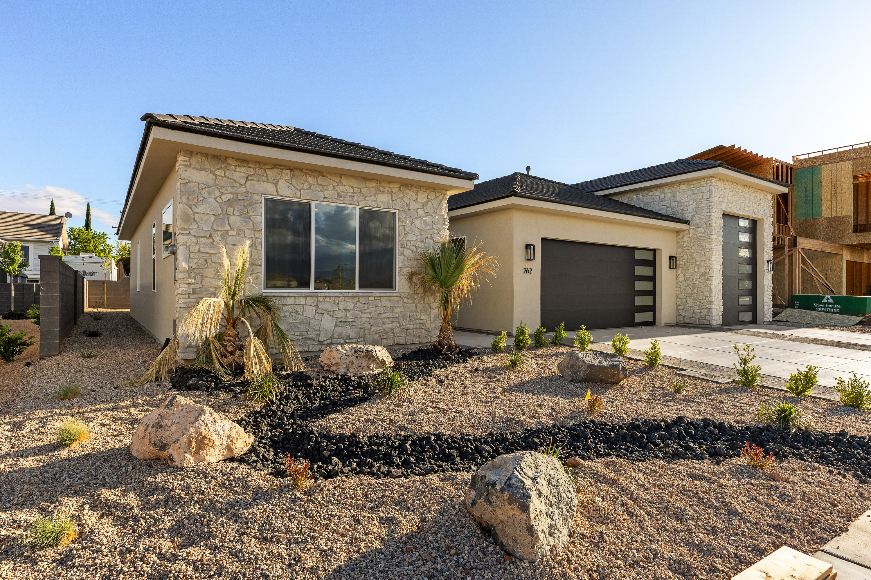 View of front of house with stone siding, an attached garage, driveway, and stucco siding