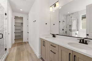 Bathroom with a marble finish shower, double vanity, light wood-style flooring, and a walk in closet