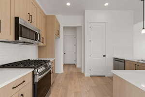 Kitchen with stainless steel appliances, tasteful backsplash, light stone counters, light wood-type flooring, and light wood finish cabinets