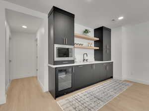 Indoor wet bar with open shelves, wine cooler, light wood-style flooring, recessed lighting, and dark cabinets