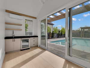 Indoor wet bar featuring dark countertops, beverage cooler, open shelves, plenty of natural light, and vaulted ceiling