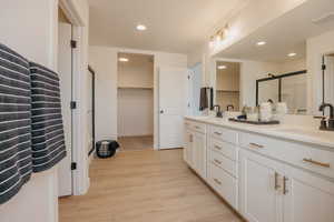 Full bath with a spacious closet, double vanity, light wood-style flooring, a stall shower, and recessed lighting