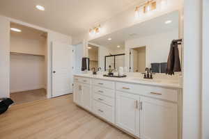 Bathroom with a spacious closet, double vanity, a stall shower, light wood-style flooring, and recessed lighting