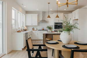 Kitchen with white cabinets, stainless steel appliances, light wood-type flooring, suspended lighting, and a center island