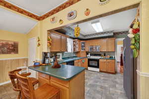 Kitchen with stainless steel appliances, wood finish cabinetry, dark countertops, a peninsula, and wainscoting