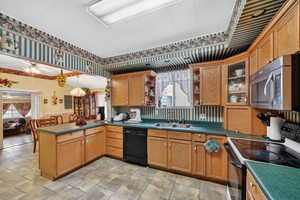 Kitchen featuring black appliances, a peninsula, open shelves, dark countertops, and a wainscoted wall