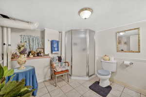 Full bath featuring a stall shower, a wainscoted wall, a textured ceiling, and tile patterned floors