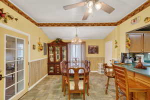 Dining space with a wainscoted wall, wooden walls, hanging lights, and a ceiling fan
