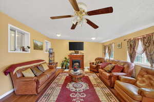 Living room with wood finished floors, a fireplace, a textured ceiling, and a ceiling fan