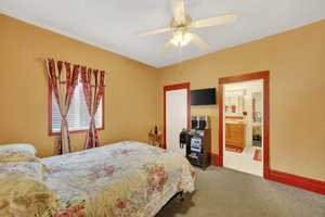 Bedroom with light colored carpet, a ceiling fan, and connected bathroom