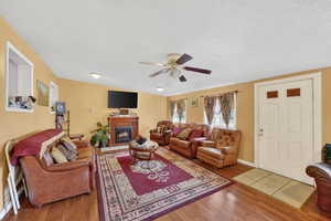 Living room featuring light wood-type flooring, ceiling fan, a glass covered fireplace, and a textured ceiling