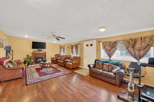 Living room featuring a glass covered fireplace, light wood-style flooring, ceiling fan, and a textured ceiling