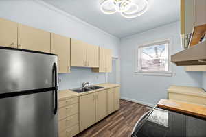 Kitchen with cream cabinets, freestanding refrigerator, crown molding, light countertops, and dark wood finished floors