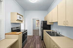 Kitchen with cream cabinets, stainless steel appliances, ornamental molding, light countertops, and dark wood-type flooring