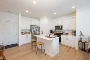 Kitchen featuring stainless steel appliances, light wood-type flooring, an island with sink, white cabinets, and recessed lighting