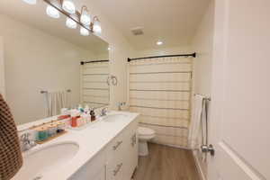 Full bath featuring double vanity, curtained shower, and light wood-type flooring