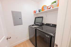 Laundry room featuring electric panel, light wood-style flooring, and washing machine and dryer