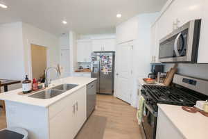 Kitchen featuring stainless steel appliances, white cabinetry, light wood-style floors, a center island with sink, and recessed lighting
