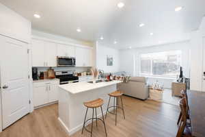 Kitchen with open floor plan, stainless steel appliances, white cabinetry, light wood-style floors, and a breakfast bar area