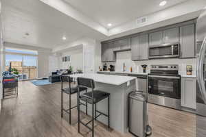 Kitchen featuring gray cabinetry, stainless steel appliances, open floor plan, a breakfast bar, and light wood-style floors