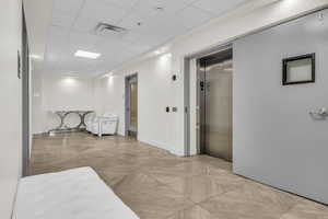 Corridor featuring a drop ceiling and elevator