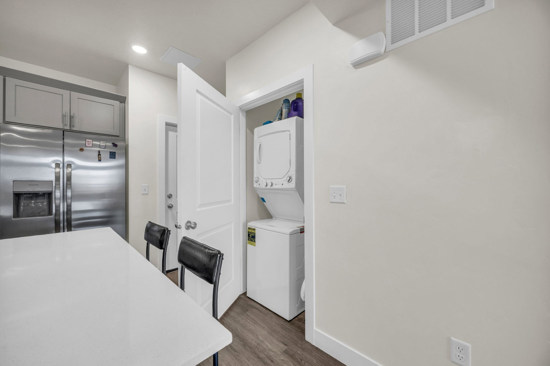 Kitchen featuring stainless steel refrigerator with ice dispenser, stacked washer and dryer, a kitchen bar, dark wood-type flooring, and gray cabinetry
