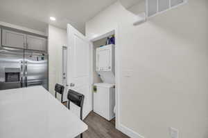 Kitchen featuring stainless steel refrigerator with ice dispenser, stacked washer and dryer, a kitchen bar, dark wood-type flooring, and gray cabinetry