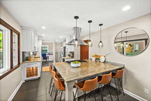 Kitchen featuring a breakfast bar, white cabinets, light stone counters, a peninsula, and island exhaust hood