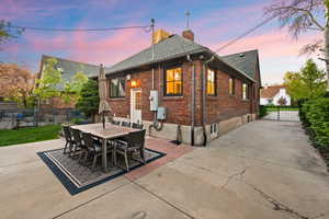 Back of house at dusk featuring brick siding, a chimney, a patio area, and outdoor dining area