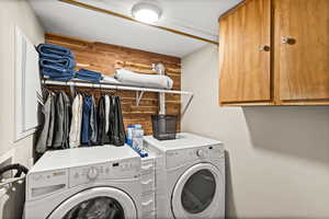 Laundry area featuring cabinet space, wood walls, a textured ceiling, and washer and clothes dryer