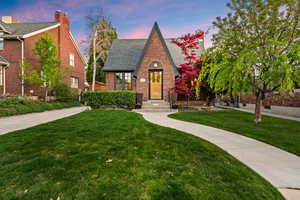 Tudor house with brick siding, a lawn, roof with shingles, and a chimney