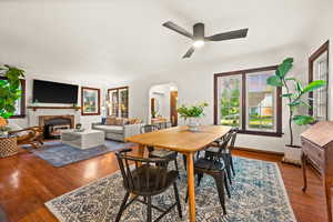 Dining room featuring arched walkways, dark wood finished floors, ceiling fan, and a glass covered fireplace