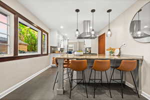 Bar area featuring light stone counters, white cabinetry, island range hood, decorative light fixtures, and wood tiled floors