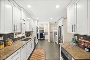 Kitchen with tasteful backsplash, light stone countertops, white cabinets, and stainless steel appliances