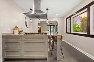 Kitchen featuring a peninsula, light stone countertops, island exhaust hood, decorative light fixtures, and arched walkways