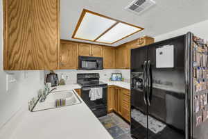 Kitchen featuring black appliances, light countertops, wood finish cabinetry, and dark stone finish flooring