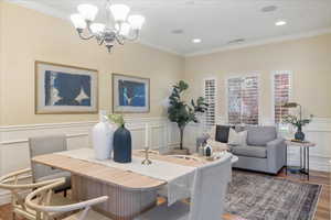 Dining area featuring ornamental molding, wainscoting, a decorative wall, dark wood-style flooring, and hanging lights