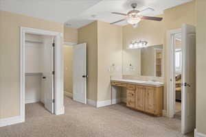 Ensuite bathroom featuring light carpet, vanity, and a ceiling fan
