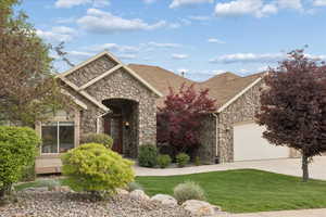 View of front facade with stone siding, a garage, concrete driveway, a shingled roof, and a front lawn