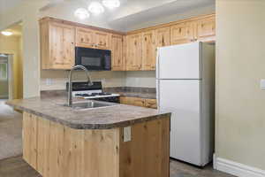 Kitchen with a peninsula, white appliances, dark countertops, and light wood finish cabinets