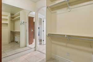 Walk in closet featuring light tile patterned floors and arched walkways