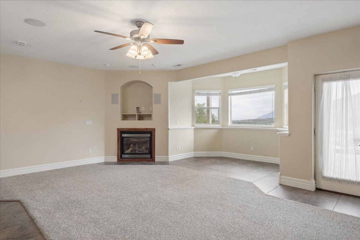 Unfurnished living room featuring light carpet, ceiling fan, a glass covered fireplace, and light tile patterned floors