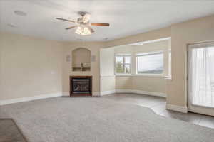 Unfurnished living room featuring light carpet, ceiling fan, a glass covered fireplace, and light tile patterned floors