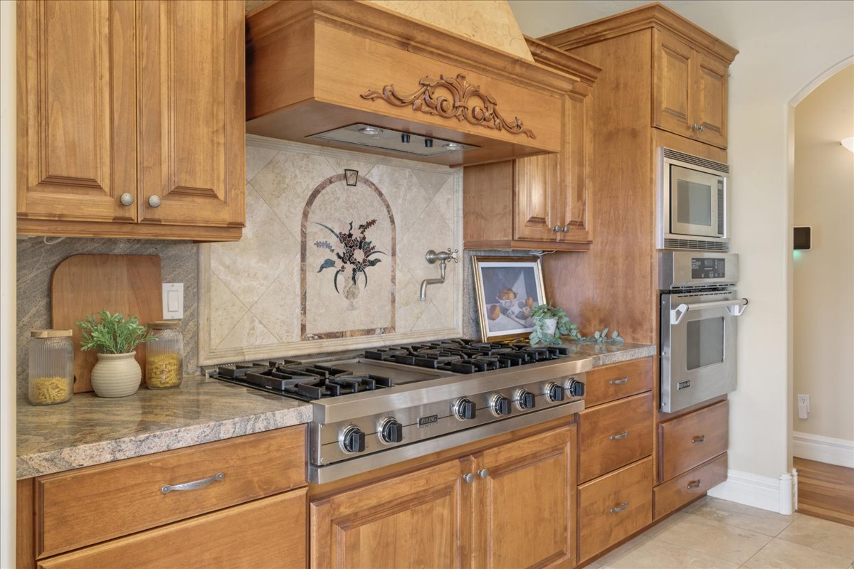 Kitchen featuring stainless steel appliances, wood finish cabinetry, arched walkways, tasteful backsplash, and light tile patterned flooring