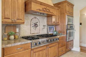 Kitchen featuring stainless steel appliances, wood finish cabinetry, arched walkways, tasteful backsplash, and light tile patterned flooring