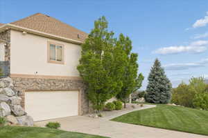 View of front of house featuring stone siding, a front yard, stucco siding, concrete driveway, and an attached garage